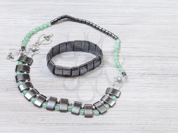 needlecraft background - handcrafted necklace from green jade, black hematite and silver beads and hematite bracelet on gray wooden board with copyspace