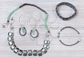 needlecraft background - handcrafted necklace and earrings from green jade, black hematite and silver beads and hematite and leather bracelets on gray wooden board