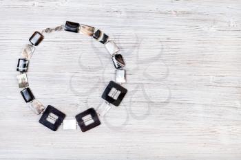 needlecraft background - top view of hand crafted necklace from horn frames, silver balls, square striped agate and nacre beads on gray wooden board with copyspace