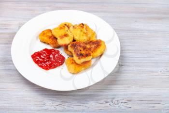 fried chicken nuggets with ketchup on white plate on gray wooden board
