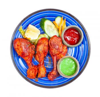 Indian cuisine - top view of portion of Tandoori chicken (spicy chicken legs marinated in yogurt and spices and roasted in tandoor) with sauces on blue ceramic plate isolated on white background