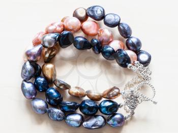 handcrafted bracelet from three stings of colored natural river pearls and silver chain and clasp closeup on pale wooden board