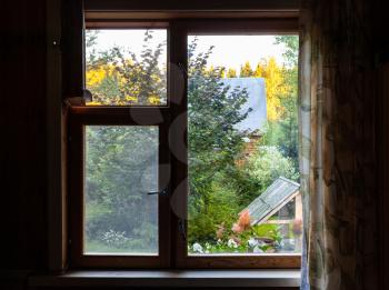 view of green backyard with well through window in rural house at summer sunset