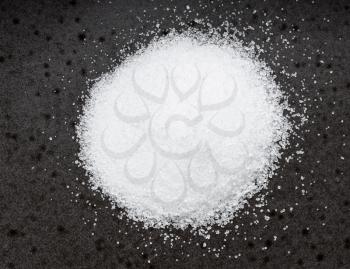 top view of pile of sugar substitute - crystalline extract of stevia plant close up on black ceramic plate
