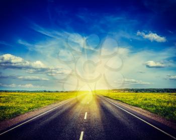 Vintage retro hipster style travel image of  travel concept background - road in blooming spring meadow on sunset