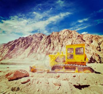 Vintage retro effect filtered hipster style travel image of Bulldozer doing road construction in Himalayas. Ladakh, Jammu and Kashmir, India