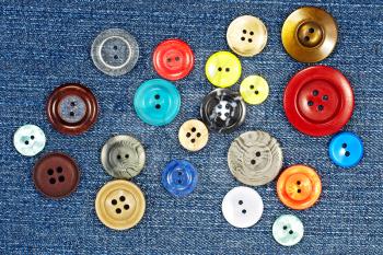 Different multicoloured buttons on blue fabric as background.