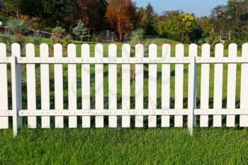 White fence on green grass against garden.