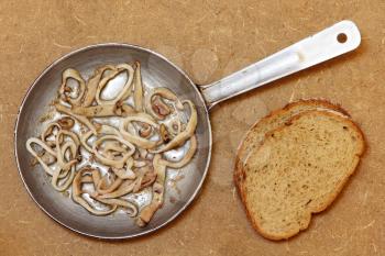 Roasted squids pieces in frying pan and bread on wooden background.Top view.