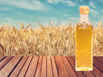 Vegetable oil on wooden table on wheat ears and blue sky background.Toned image.