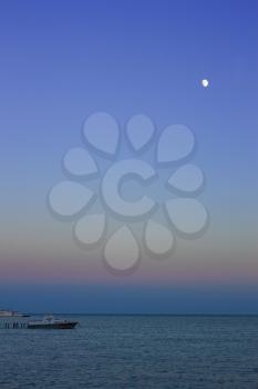 Night at sea. The moon in the cloudless sky illuminating motor boats near a pier