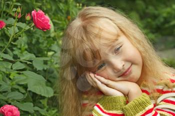 Beautiful small Caucasian girl in park near the rose bush