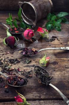 Dry tea leaves in spoons with small buds of roses in  wooden box