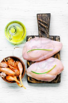 raw chicken fillets on cutting wooden board with onions and olive oil