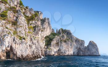 Small touristic motorboat enters near the grotto in coastal rocks of Capri island, Italy