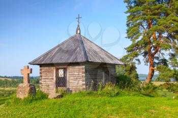Ancient small wooden Orthodox chapel and stone cross on Savkina gorka, Pskov Region, Russia
