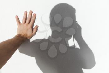 Man touching his shadow on white wall and taking photo