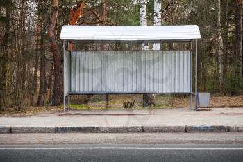 Small empty bus stop building stands on the roadside in the forest