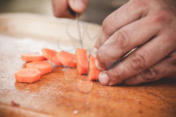 Slicing of a raw carrot. Cook hands with knife, close-up photo with selective focus