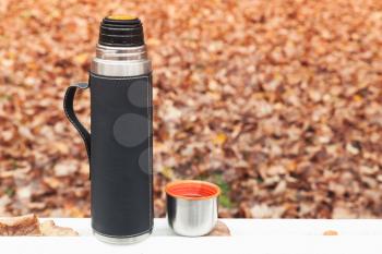 Stainless steel vacuum tourist thermos stands on white table in autumn park