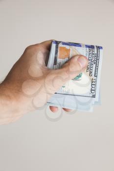 Bundle of One Hundred Dollars notes in male hand over gray wall background