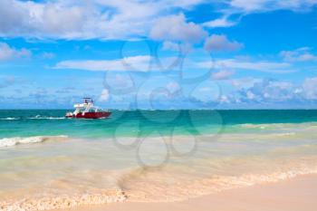 Coastal Caribbean landscape. Red motorboat goes near Atlantic ocean coast, Hispaniola island, Dominican republic. Bavaro beach