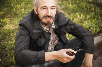 Young smiling bearded man smoking pipe in summer park, outdoor portrait