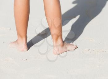 Wet female feet stand on white coastal sand in the sunlight