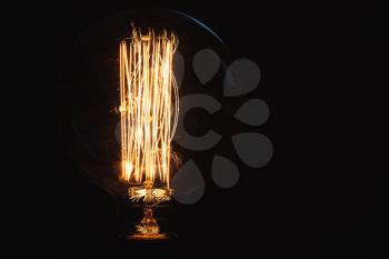 Vintage stylized large tungsten lamp glowing over dark background, close-up photo with selective focus and shallow DOF