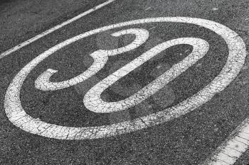 30 km per hour. Round speed limit road marking on dark gray asphalt