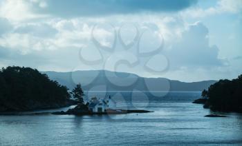 Dark Norwegian coastal landscape with small wooden houses on isle. Blue tonal filter effect