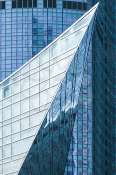 Modern architecture, abstract vertical fragment, sharp corner made of glass and steel with reflections of blue sky
