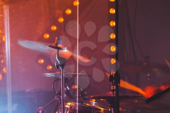 Live rock music colorful background, drummer plays with drumsticks on rock drum set. Warm toned closeup photo, soft selective focus