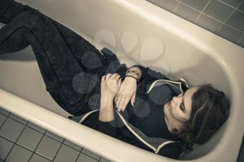 Sad stressed Caucasian teenage girl laying in empty shower bath. Depression mood concept. Warm vintage tonal correction photo filter