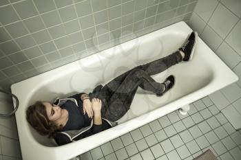 Sad stressed European teenage girl laying in empty shower bath. Depression mood concept. Vintage tonal correction photo filter
