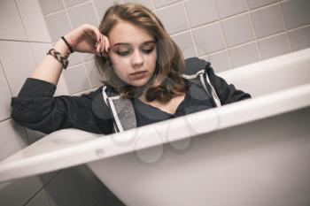 Stressed sad Caucasian teenage girl sitting in bath. Depression mood concept. Vintage tonal correction photo filter