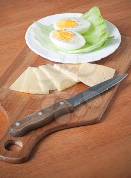 Simple breakfast background with knife, cheese and boiled egg on cutting board