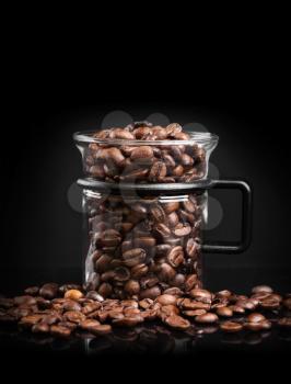 Mug made of glass with roasted coffee beans on black background