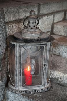 Old metal outdoor lamp with red burning candle stands on stone stairs
