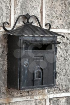Old weathered black metal mailbox mounted on gray stone wall