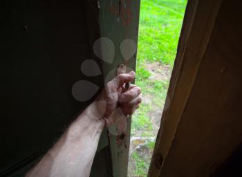 Hand of a man opening old door from the dark room into the fresh green scene. Back to the nature metaphor