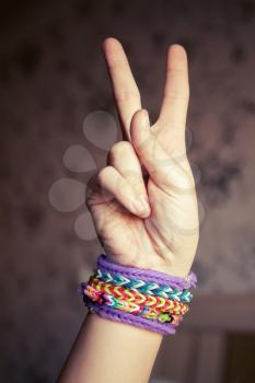Child hand showing victory sign with colorful rubber rainbow loom bracelets on wrist, trendy teenagers fashion accessories. Vintage retro tonal photo filter correction