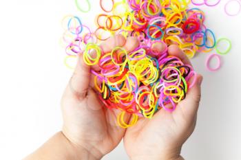 Little child hands and pile of small round colorful rubber bands for making rainbow loom bracelets on white background