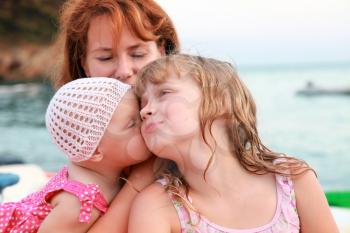 Young Caucasian family on the sea coast. Young mother with her kissing daughters