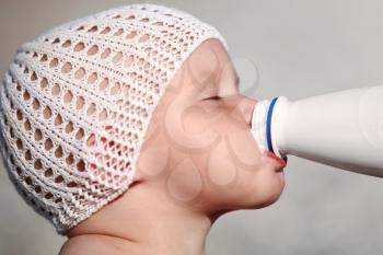 Little Caucasian baby drinks milk from the white bottle