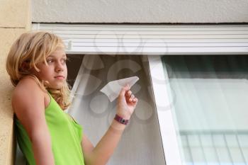 Little blond Caucasian girl with paper plane in window, outdoor closeup portrait