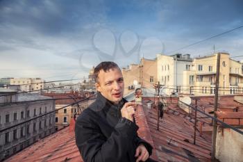 Young Caucasian man smokes cigar on the roof in central part of St.Petersburg, Russia