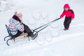 Little baby girl in pink pulling a sled on snowy road