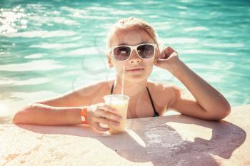 Little blond happy girl with glass of cocktail in swimming pool