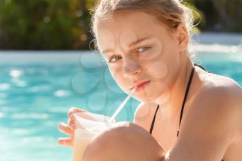 Little blond girl drinks cocktail in swimming pool
